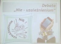 Zdjęcie slajdu z napisem: Debata ,,Nie - uzależnieniom&quot;. Z lewej strony tematyczny rysunek but depczący butelkę i strzykawki, a po prawej stronie dłonie opętane łańcuchem z kłódką, a w nich telefon komórkowy.