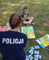 Policjantka tłumaczy dzieciom zasady gry edukacyjnej ,,Bezpieczne wakacje&quot;