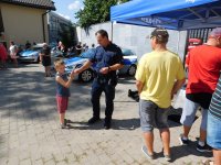 Na placu zewnętrznym przy Komendzie Powiatowej  Policji w Zambrowie, uczestnicy spotkania zapoznają się ze sprzętem służbowym. Policjant przekazuje odblask dziecku.