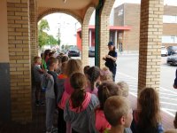 Przed budynkiem szkoły, Policjantka omawia zasady bezpieczeństwa zgromadzonym uczniom.