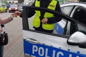 Policjant zambrowskiej drogówki przekazuje odblask kobiecie. Oboje stoją przy oznakowanym radiowozie.