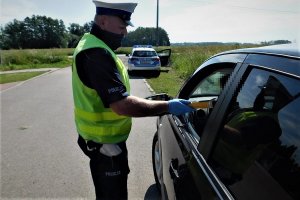 Policjant ruchu drogowego podczas sprawdzania stany trzeźwości kierowcy siedzącego w pojeździe. W tle radiowóz policyjny.