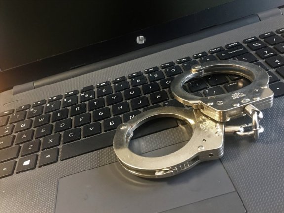Na klawiaturze laptopa leżą policyjne kajdanki.