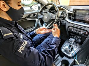 Policjantka siedząca w radiowozie podczas dezynfekcji dłonie.