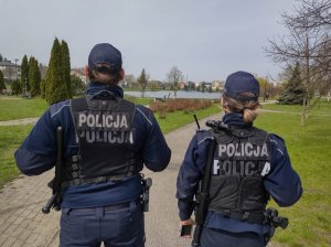 Umundurowani policjanci podczas patrolu w parku. Stojący tyłem do zdjęcia.