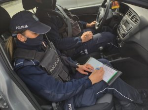 Umundurowana policjantka siedząca w radiowozie podczas pisania mandatu.