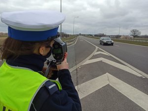 Policjantka ruchu drogowego podczas pomiaru prędkości pojazdu. W tle jezdnia.