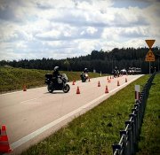 Widok na drogę dwujezdniową. Pasy jezdni rozdzielone zielenią, na jezdni rozstawione słupki. Motocykliści jeżdżą pomiędzy słupkami slalomem.