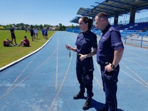 Policjant oraz policjantka trzymająca stoper na stadionie.