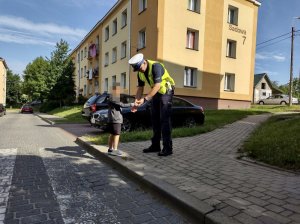 Policjant zakładający na dłoń dziecka odblask. W tle osiedle.