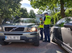 Policjanci podczas kontroli samochodu koloru srebrnego stoją przy drzwiach kierowcy.