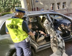 Policjant daje dziecku odznakę, który siedzi w foteliku samochodu.