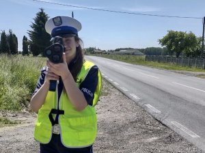 Policjanta stojąca przodem podczas pomiaru prędkości. W tle ulica.