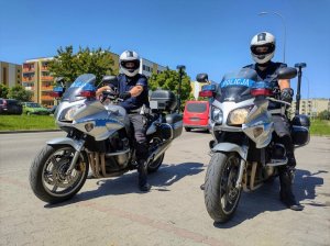 Dwóch policjantów na motorach policyjnych na parkingu. W tle osiedle.