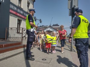 Policjant rozdaje przedszkolakom odblaski oraz rozmawia.