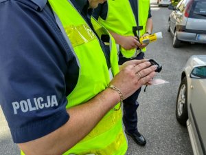 Dłonie dwóch policjantów. Jeden z nich trzyma alkoblow, a drugi prawo jazdy i urządzenie służbowe.