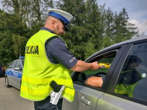 Policjant podczas badania stanu trzeźwości kierującego siedzącego w białym samochodzie.