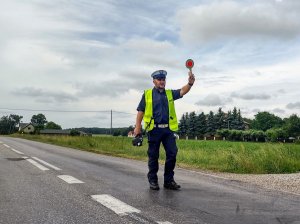 Policjant stojący na drodze z podniesioną tarczą dający polecenie kierującemu do zatrzymania.