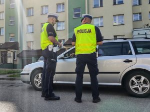 Policjanci stojący tyłem podczas kontroli pojazdu.