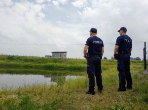 Policjanci podczas kontroli zbiornika wodne, który jest w tle.