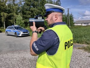 Policjantk ruchu drogowego podczas wykonywania pomiaru prędkości. W tle radiowóz.