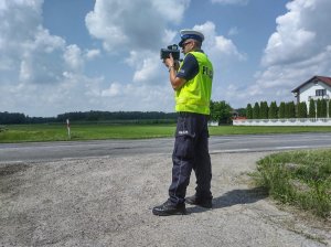 Umundurowany policjant wydziału ruchu drogowego podczas pomiaru prędkości. W tle jezdnia.