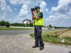 Umundurowany policjant wydziału ruchu drogowego podczas pomiaru prędkości. W tle jezdnia.