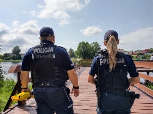 Dwójka policjantów na moście podczas patrolowania akwenu wodnego.