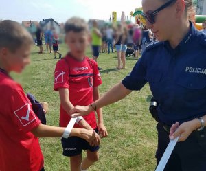 Policjanta zakładająca dziecku odblask na rękę.