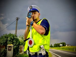 Policjant podczas pomiaru prędkości. W tle jezdnia.