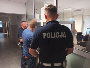 Zatrzymany nietrzeźwy kierowca podczas badania stanu trzeźwości, obok stoją policjanci.