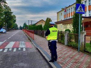 Policjant stojący na chodniku przed przejściem dla pieszych przy szkole.