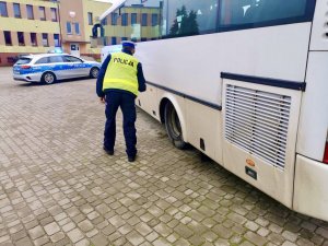 Umundurowany policjant podczas kontroli autobusu. W oddali radiowóz.