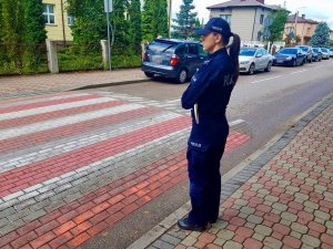 Umundurowana policjantka stojąca przed przejściem dla pieszych i obserwująca ruch.