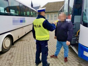 Umundurowany policjant podczas kontroli trzeźwości kierowcy autobusu. Obok zaparkowane autobusy.