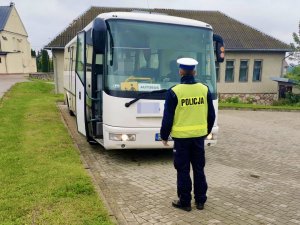 Umundurowany policjant podczas kontroli autobusu stojący przed nim.