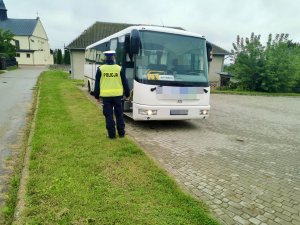 Umundurowany policjant podczas kontroli autobusu, stojąc przed nim.