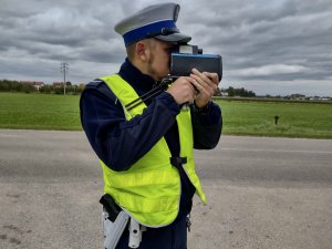 Policjant podczas pomiaru prędkości. W tle jezdnia oraz pola.