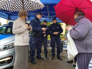 Policjanci podczas rozmowy z seniorami. Policjant rozdaje ulotki.