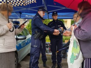 Policjanci podczas rozmowy z seniorami. Policjant rozdaje ulotki.