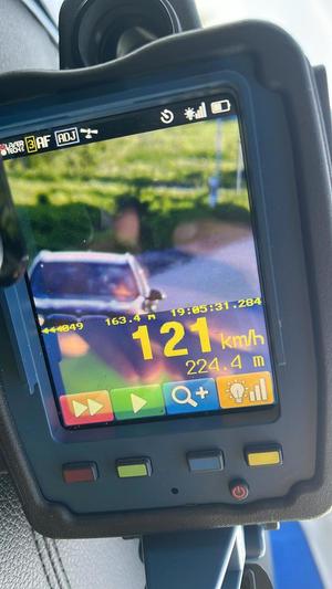 Ekran ręcznego miernika prędkości wskazujący prędkość jadącego pojazdu 121 kilometrów na godzinę.