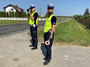 Dwóch umundurowanych policjantów podczas kontroli prędkości kierowców na drodze.