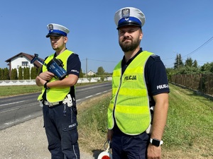 Dwóch umundurowanych policjantów podczas kontroli prędkości kierowców na drodze.