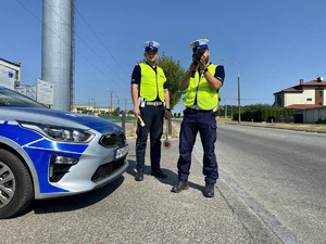 Dwóch umundurowanych policjantów podczas kontroli prędkości kierowców na drodze.