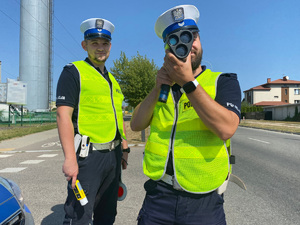 Dwóch umundurowanych policjantów podczas kontroli prędkości kierowców na drodze.