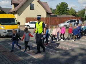 Umundurowany policjant podczas przeprowadzania dzieci przez przejście dla pieszych.