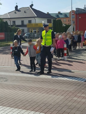 Umundurowany policjant podczas przeprowadzania dzieci przez przejście dla pieszych.