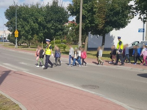 Umundurowani policjanci podczas przeprowadzania dzieci przez przejście dla pieszych.