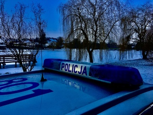 Dach radiowozu, a w tle zaśnieżony park.