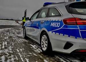 Radiowóz stojący na poboczu, a w tle policjant.